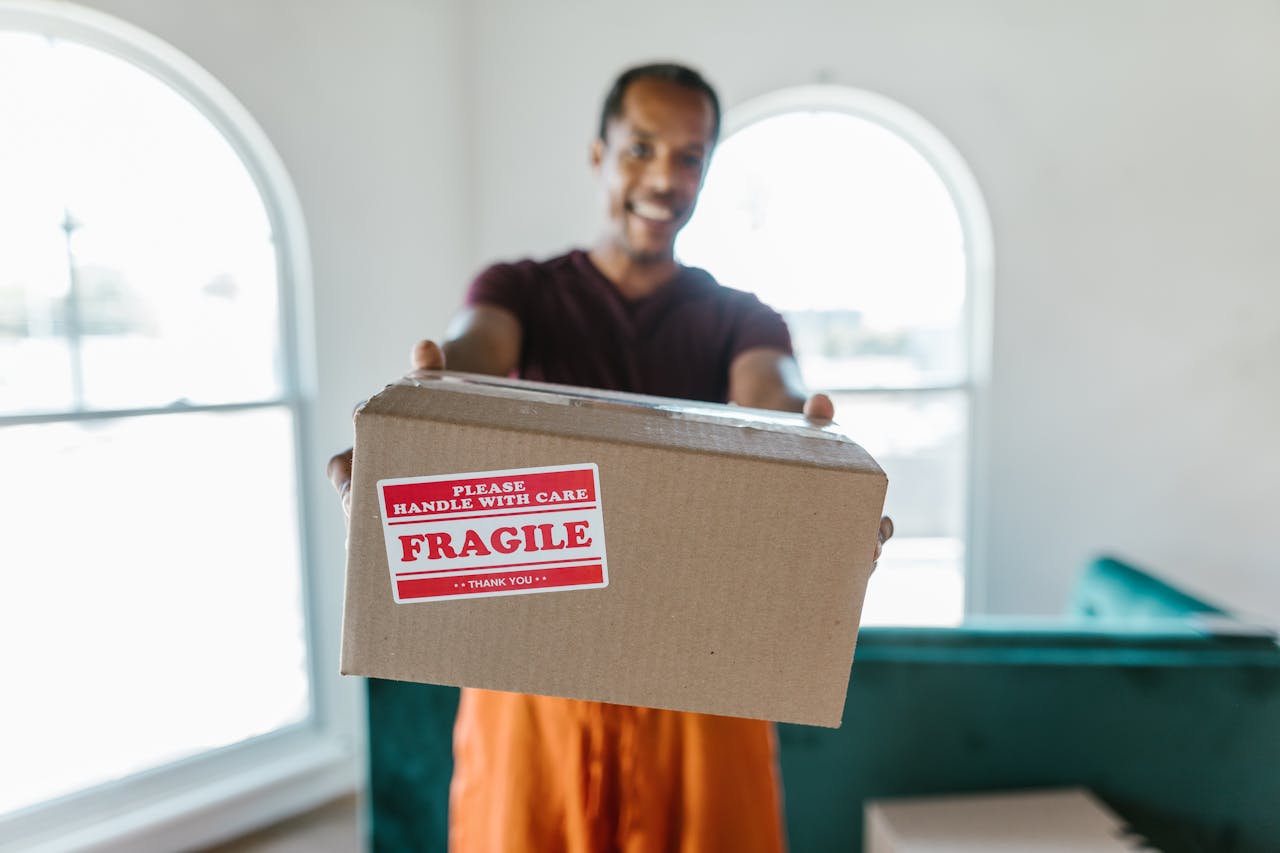services-03 A person holding a cardboard box labeled fragile, signifying careful handling during a move.