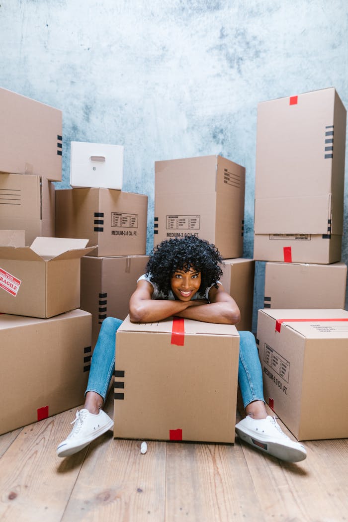 A cheerful woman surrounded by stacked moving boxes, ready to setup her new home.